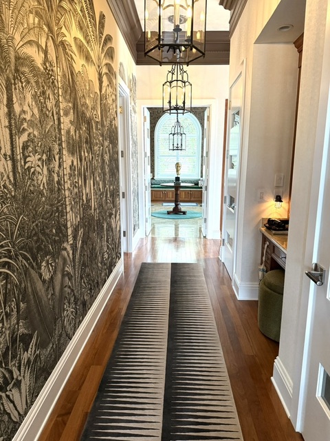 Elegant estate hallway with tropical mural wallcovering, warm wood flooring, striped runner, lantern pendants, and a view into the room beyond