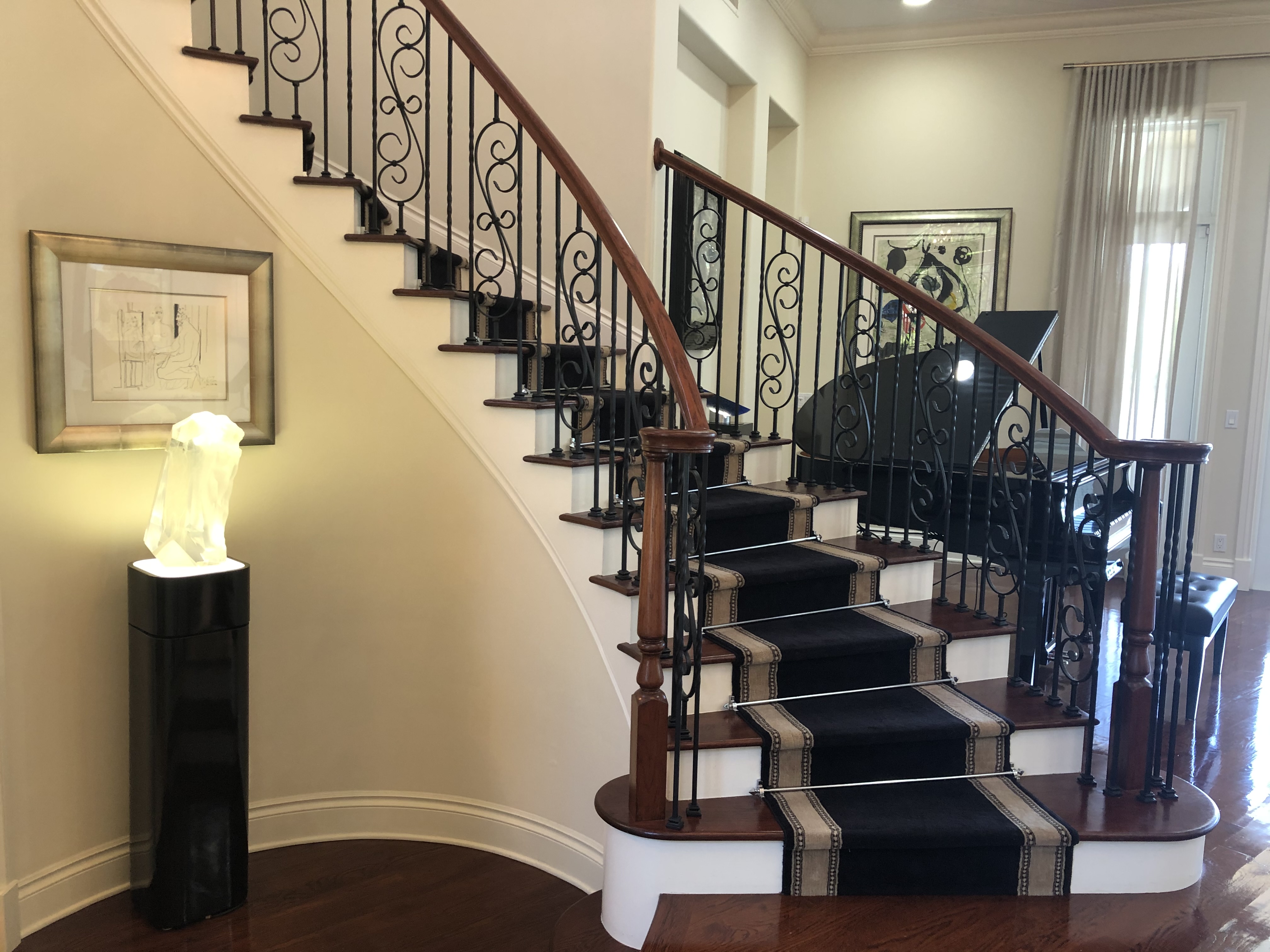 Curved stair with iron railing and grand piano nearby